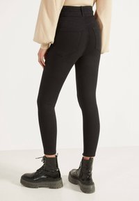 Jeans negros de tiro alto y ajustados con bolsillos traseros, combinados con botas de combate de charol negro con suela gruesa.