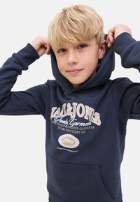 Marineblaues Hoodie aus weichem Material, mit einer Fronttasche und einem grafischen Logodesign mit Text, darunter "1990" und "Quality Garments."