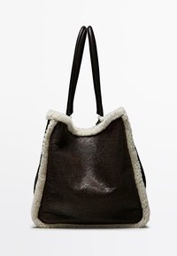 Bruine leren draagtas met een zachte witte fleece rand, voorzien van twee donkere handgrepen en een ruime, gestructureerde vorm. Gedetailleerd met een textuur aan het oppervlak.