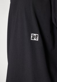 Černá látka s malým, čtvercovým výšivkou loga Nike, které zobrazuje stylizované písmeno "N" a slovo "NIKE" diagonálně napříč.