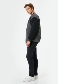 Chaqueta varsity gris y negra con cierre de botones, puños acanalados y bolsillos laterales. Llevarla sobre jeans oscuros y zapatillas blancas.