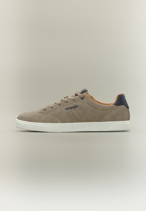Beżowy niski sneaker z białą podeszwą, granatową pętlą przy pięcie, perforowanymi bocznymi panelami, sznurówkami i logo „Wrangler” po boku.