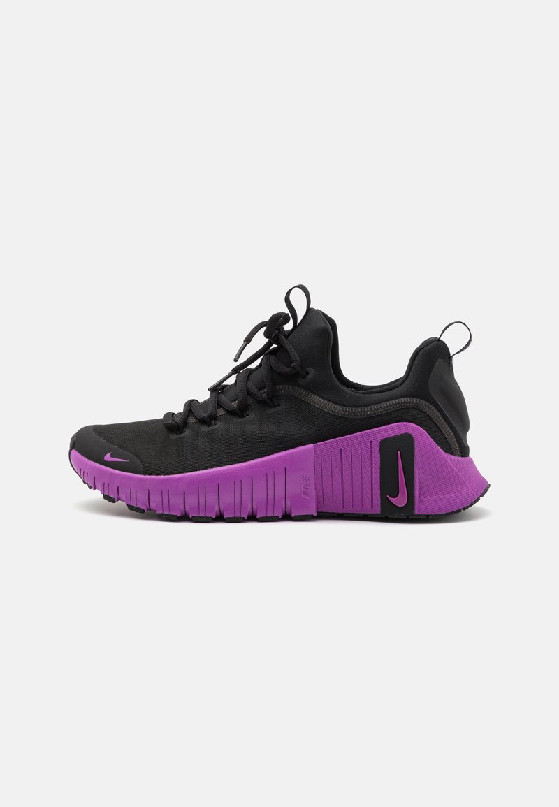 Pantof cu un design sportiv de culoare neagră, cu un superior dintr-o țesătură texturată, talpă din cauciuc violet și un model de aderență pronunțat. Include șireturi și un mic logo Nike.