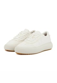 Zapatillas de lona blancas con parte superior texturizada, puntera redonda y suela de goma. Presenta una marca mínima y una suela de goma de color contrastante.