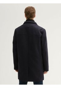 Abrigo de mezcla de lana de un azul marino oscuro, con un cuello alto, forma ajustada y mangas largas. Presenta una costura en la parte posterior y un dobladillo recto.