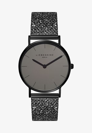 Rund ur med en grå skive, sorte timemarkører og et struktureret sort glimmerrem. Finishen er elegant, med et enkelt design og mørke accenter.