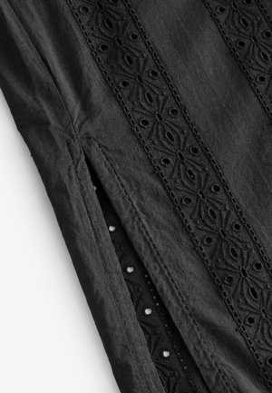 Tessuto nero con ricami intricati e motivi a taglio. La texture è liscia, con una leggera lucentezza e spacchi laterali per un dettaglio di design.