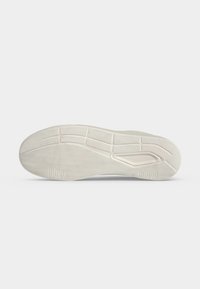 Semelle d'une sneaker blanche avec des motifs de grip texturés et une semelle segmentée pour la traction, présentée sur un fond clair uni.