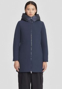 Manteau bleu marine avec un col haut et volumineux ; tissu lisse ; manches longues ; fermeture éclair à l'avant ; poches latérales ; design minimaliste.