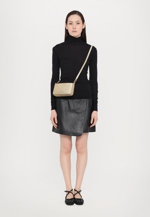 Svart polotröja, svart läderskjol, guld crossbody-väska och svarta skor med remmar och dekorationer. Enkel design, neutrala färger.