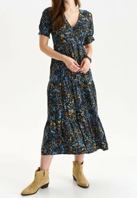 Vestido de estampado floral con un escote en V pronunciado, mangas cortas y una falda en capas. Los colores incluyen azul, negro, naranja y amarillo. Combinado con botas de tobillo beige.