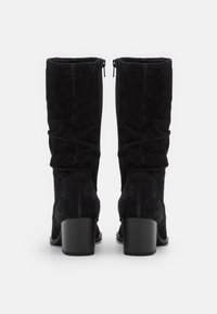 Bottes montantes en daim noir avec un design légèrement froncé, dotées d'une fermeture éclair et d'un talon bloc. Texture lisse, sans motifs visibles.