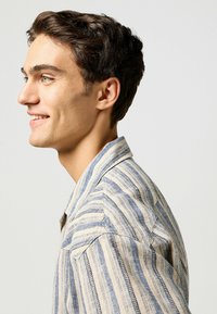 Gestreept overhemd in beige en blauwe tinten, met een kraag, textuurstof en zichtbare stiksels langs de naden.