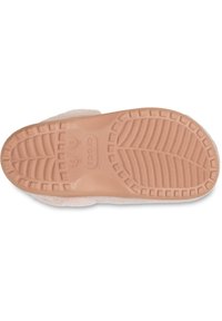 Semelle en caoutchouc rose d'une chaussure de maison avec un motif de texture antidérapant, présentant un bord supérieur doux et duveteux. Marquages de taille visibles sur la semelle.