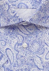 Camicia bianca con motivo paisley blu, caratterizzata da un colletto classico e un singolo bottone bianco sul davanti, texture liscia e design dettagliato.