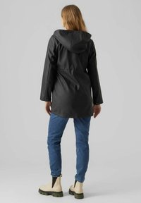 Zwarte waterdichte jas met een capuchon, lange mouwen en een relaxte pasvorm, gecombineerd met blauwe jeans en beige enkellaarzen. Geef een gladde textuur.