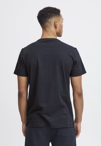 Camiseta de algodón negra con cuello redondo clásico y mangas cortas, que presenta un dobladillo recto y una textura suave. Sin logotipos ni patrones visibles.