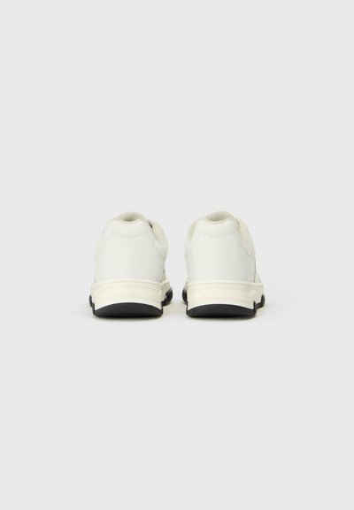 Weiße Sportschuhe mit glattem Lederoberteil, gepolstertem Kragen und schwarzer Gummisohle. Minimalistisches Design ohne auffällige Muster oder Akzente.