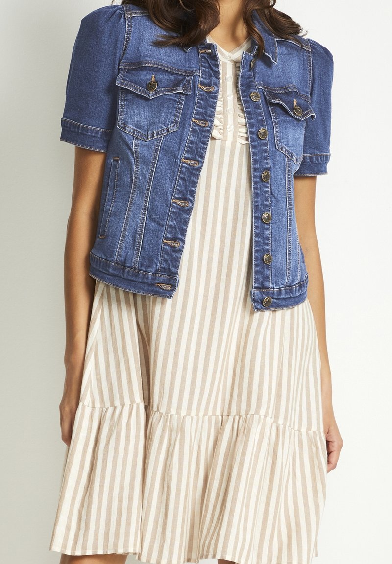 Jeansjacka med korta ärmar, två bröstfickor och knappar i guldton, kombinerad med en randig klänning i beige och vitt med en volangnederdel.