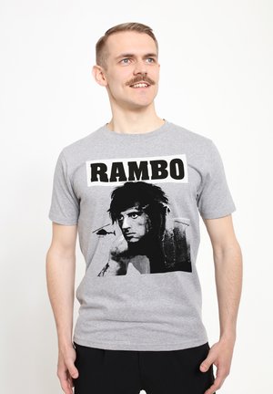 Šedé bavlněné tričko s černobílým grafickým potiskem postavy a textem "RAMBO" v tučných černých písmenech nahoře.