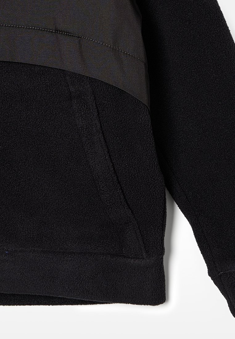 Felpa in pile nera con un pannello in tessuto liscio grigio sulla parte superiore del torace. Presenta una tasca frontale e un tessuto testurizzato.