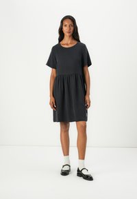 Kurzes, graues Kleid mit lockerem Schnitt, geraffter Taille und glattem Stoff. Mit einem dezenten Seitenetikett akzentuiert.