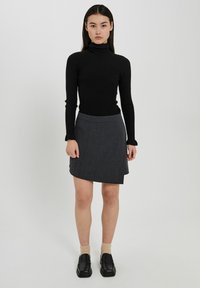 Maglione a collo alto nero a coste, gonna avvolgente grigia, scarpe nere basse e calzini color carne. L'outfit presenta un look moderno e stratificato.