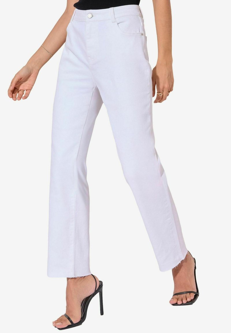 Los pantalones de mezclilla blancos de pierna recta presentan una cintura alta, cierre frontal con botón, trabillas para cinturón y dobladillos deshilachados. Combinados con tacones negros de tiras.