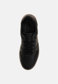 Baskets en cuir noir avec bout arrondi, design à lacets, dessus texturé et logo sur le côté. Semelle en caoutchouc blanche visible en dessous.