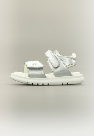 Ασημένιο και λευκό παιδικό σανδάλι με δύο ρυθμιζόμενα λουράκια με βέλκρο και χοντρή, αυλακωτή σόλα σε ουδέτερο φόντο.