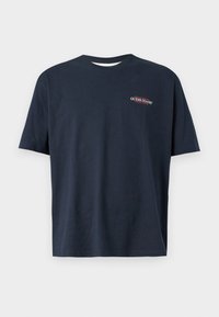 Tengerészkék pamut póló rövid ujjakkal. Az elején kis hímzett "GUESS JEANS" logó található piros és fehér színben. Kerek nyakkivágás, normál fazon.