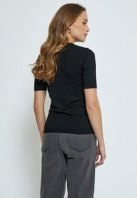 Top negro de manga corta con diseño ajustado y dobladillo acanalado, combinado con pantalones grises de tiro alto que presentan bolsillos traseros y detalles de costura.