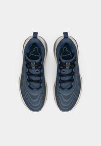 Baskets de sport bleu marine avec une texture ondulée, lacets noirs et une semelle claire. Présentent un logo sur la languette et un col rembourré.