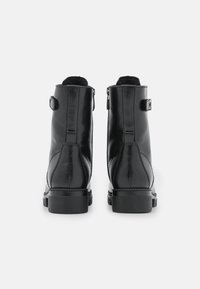 Bottines en cuir noir avec une finition lisse, présentant un détail en boucle et un talon bloc robuste, vues de l'arrière.