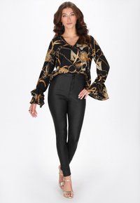 Fekete blúz arany láncmintával, fodros ujjakkal; szűk fekete nadrággal és arany pántos magassarkúval párosítva. Simaságú anyag, testhezálló szabás.