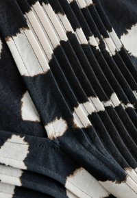 Tela de patrón en blanco y negro con pliegues. El diseño presenta formas y texturas irregulares, combinando secciones lisas y acanaladas.