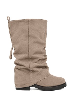 Beige suède laars tot halverwege de kuit met een slordig design, afgeronde neus, zwarte platte zool en trekriem aan de achterkant.