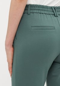 Groene stretchbroek met een elastische tailleband, een gladde textuur en een enkele achterzak met een plat ontwerp.