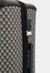 Black and white patterned suitcase with geometric design, gold accents, dual zippers, and a combination lock feature.