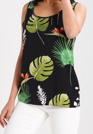 Mouwloos zwart topje met grote groene tropische bladeren en oranje bloemen, gedragen met witte broek.