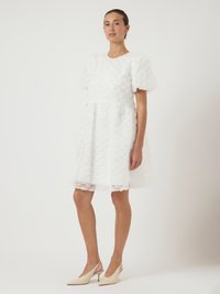 Λευκό φόρεμα με υφή ροζέτας, κοντά φουσκωτά μανίκια, εφαρμοστή μπλούζα και φουσκωτή φούστα. Συνδυασμένο με μπεζ πέδιλα slingback.