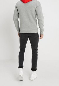 Grå sweatshirt med röd huva, kombinerad med mörka jeans och vita sneakers. Har en kroppsnära design och ribbade cuffs på ärmarna.