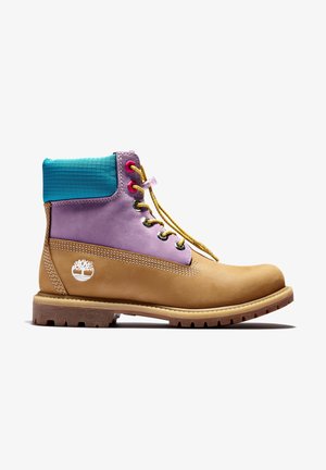 Botte de travail beige avec section médiane en cuir violet, col rembourré turquoise au niveau de la cheville, lacets jaunes et semelle marron robuste, logo Timberland sur le côté.
