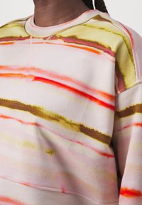Sudadera de algodón con base en rosa pastel y rayas abstractas en amarillo, naranja, rojo y marrón. Cuello y puños acanalados.