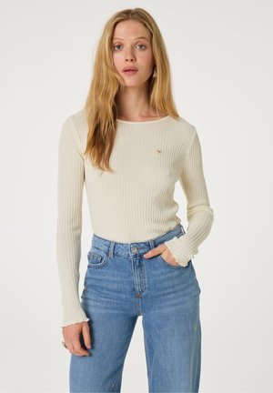 Crème ribbed langemouwshirt met een ronde halslijn en subtiele hartdetails, gecombineerd met high-waisted blauwe spijkerbroek.