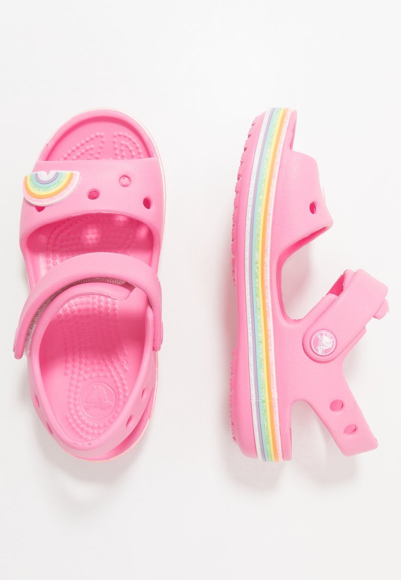 Vaaleanpunaiset lasten sandaalit, jotka on valmistettu kevyestä kumista. Niissä on sateenkaariaskartelu, säädettävä hihna ja värikkäät raidoitetut pohjat.