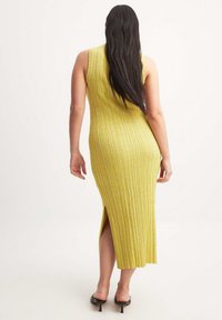 Robe sans manches en maille côtelée jaune avec une fente latérale, longueur mi-mollet, présentant une coupe ajustée et une texture lisse.