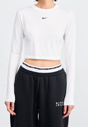 Biały, długi rękaw crop top z czarnym logo Nike. W połączeniu z luźnymi czarnymi dresami z białym paskiem z logo marki.