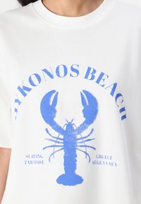 Balta medvilninė marškinėliai su mėlynu omaro grafiką ir tekstu "MYKONOS PAPLODIS," "SURIETI RAJONAS," "GRAIKIJA," ir "AEGEJOS JŪRA."