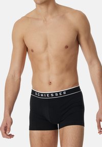 Boxer neri realizzati in tessuto morbido. Presentano un elastico bianco con il logo "SCHIESSER". Design aderente con taglio dritto.